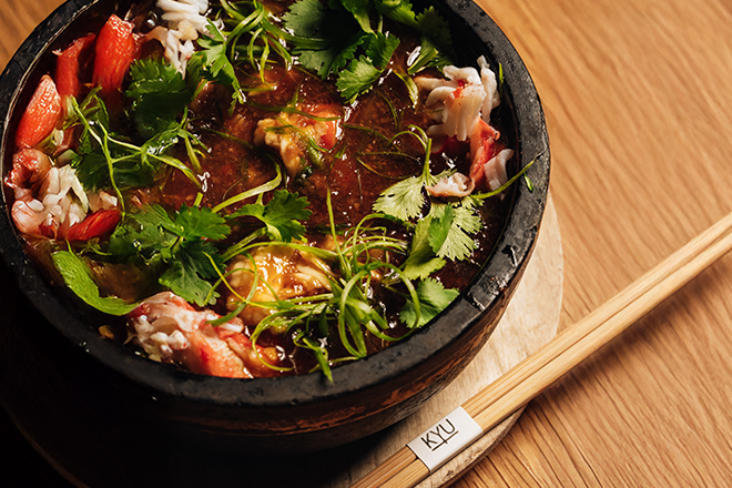 Bowl of food sitting on a wooden table with chopsticks with KYU logo