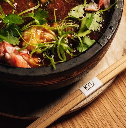 Bowl of food sitting on a wooden table with chopsticks with KYU logo