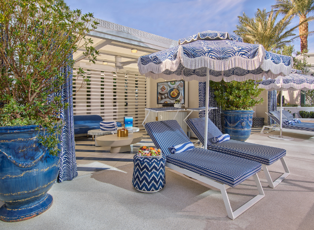 Outdoor seating area with umbrellas, lounge chairs, foliage, couches, and tables.