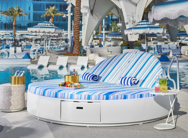 Daybed next to a pool with towels, champagne bottle, fruit tray and juice vase.