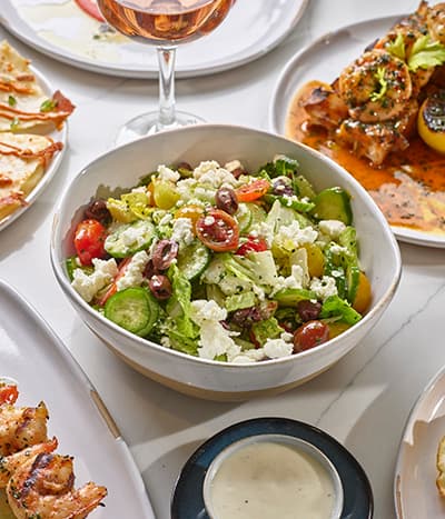 Bowl of salad in the center of several plates of food.