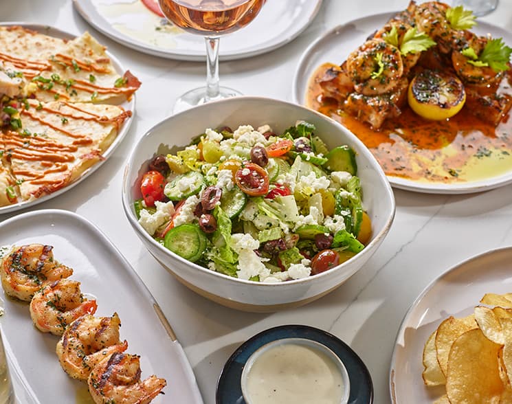 Bowl of salad in the center of several plates of food.