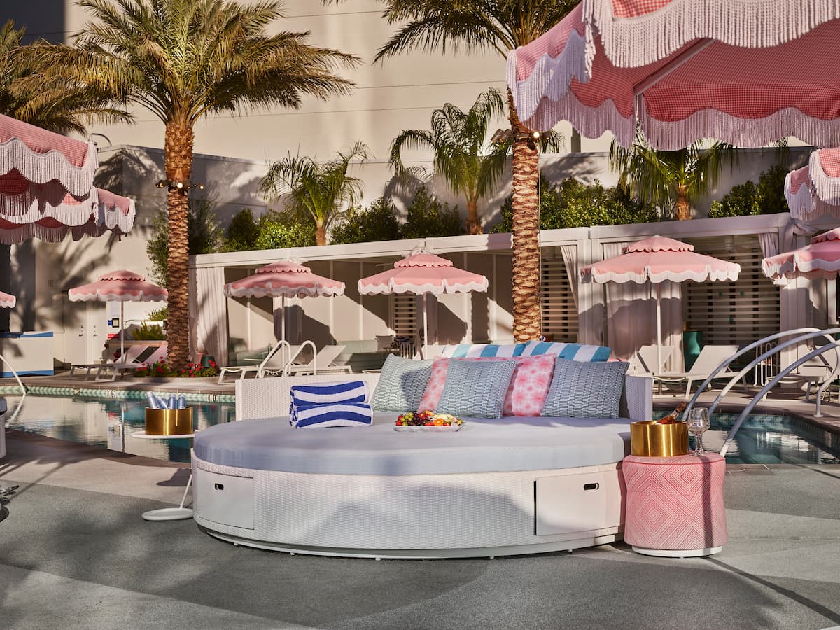 Daybed with lounge chair, umbrella, towels, bottles, champagne, fruit tray and pink accents