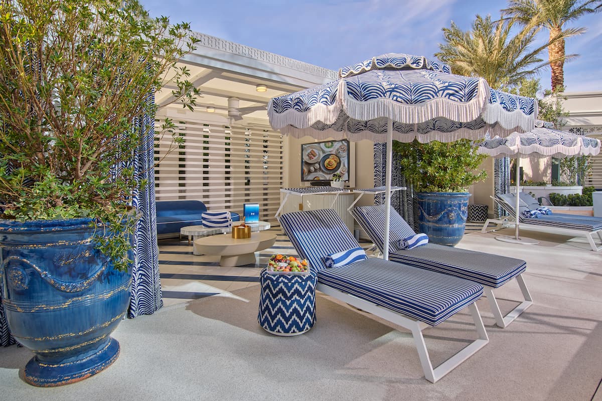 Outdoor seating area with umbrellas, lounge chairs, foliage, couches, and tables.