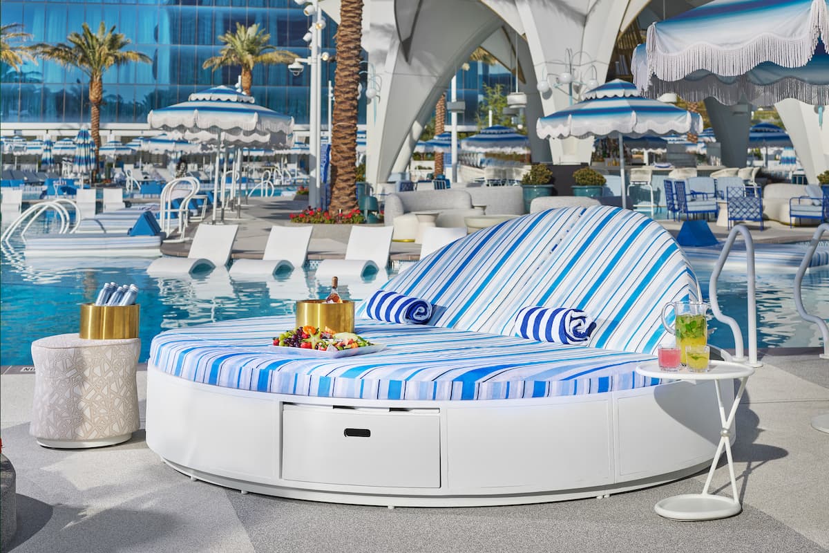 Daybed with blue stripes, towels, fruit tray, champagne holder, fruit juice next to a pool