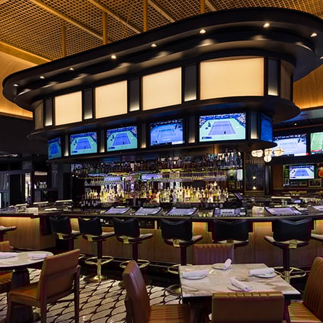 Oblong bar with televisions surrounded by stools, tables and chairs in The Tavern