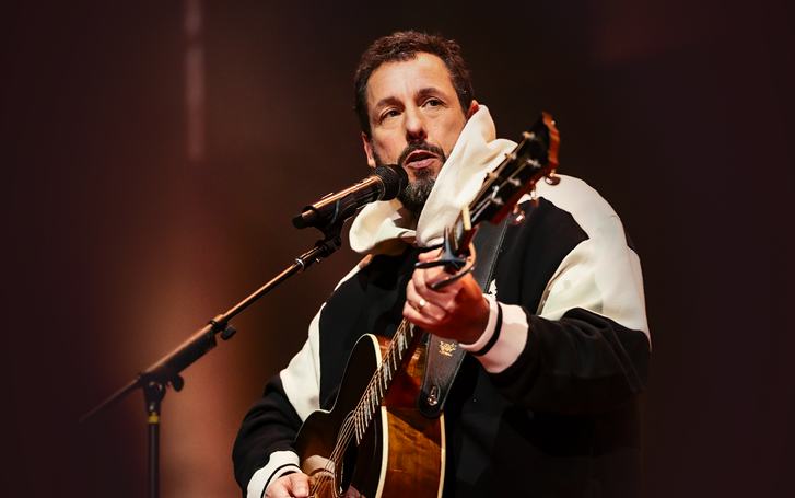 Adam Sandler at a mic holding a guitar