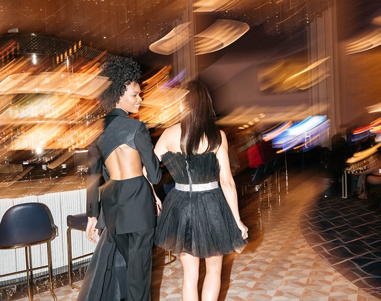 Pair of women in evening dresses walking through a deliberately blurred background in Bleau Bar