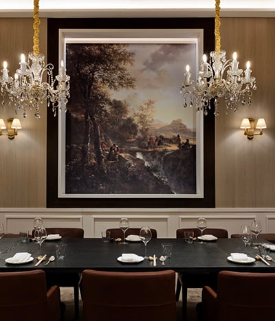 6-person black dining table with brown chairs and place settings underneath 2 chandeliers with a painting on the back wall surrounded by 2 sconces at Chyna Club restaurant