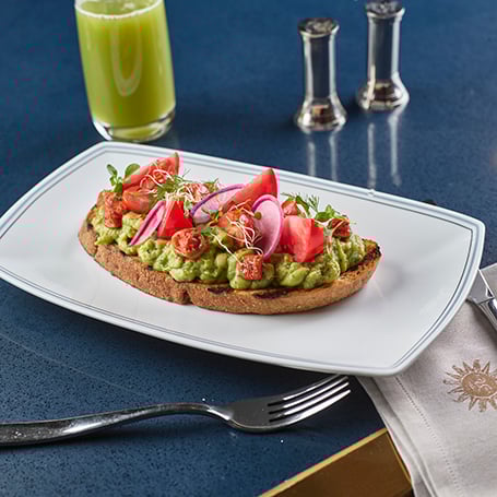 Plate of avocado toast on white plate and blue table in Vida