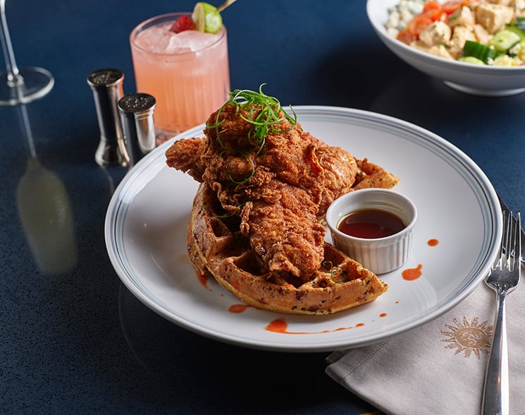 Plate of chicken and waffles on a white plate on a blue table in Vida