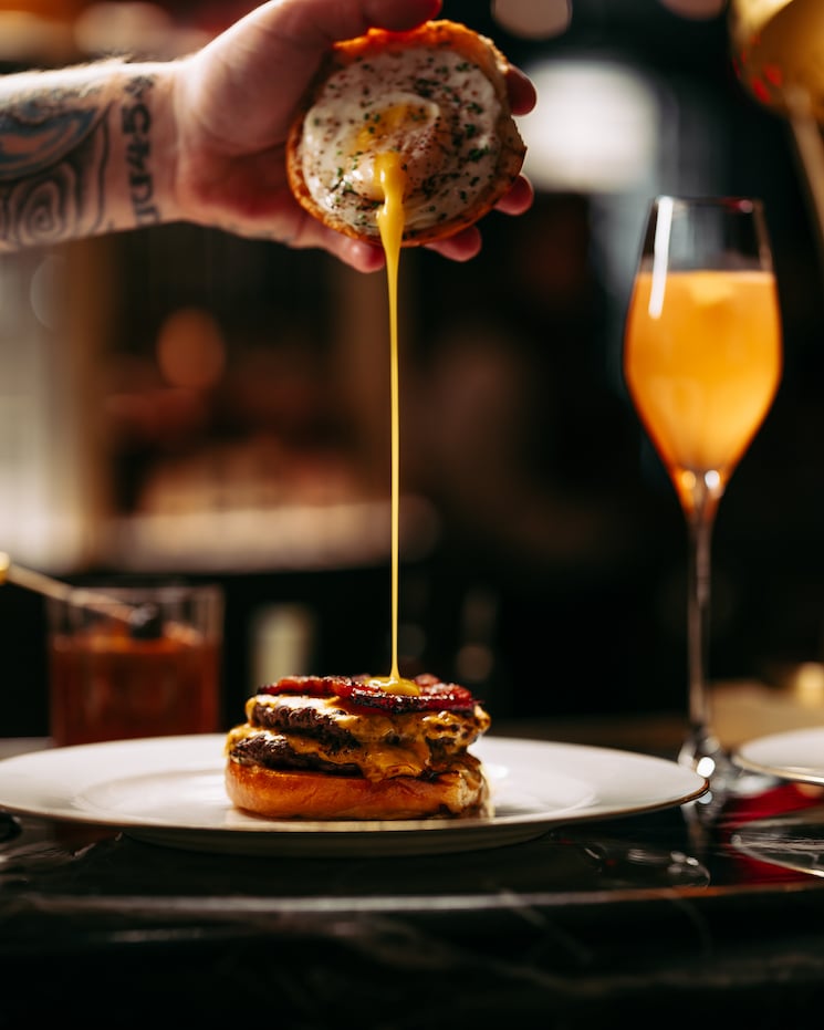 Hand holding egg pouring over burger