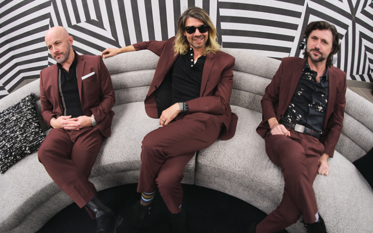 3 members of Taking Back Sunday in maroon suits on a grey couch