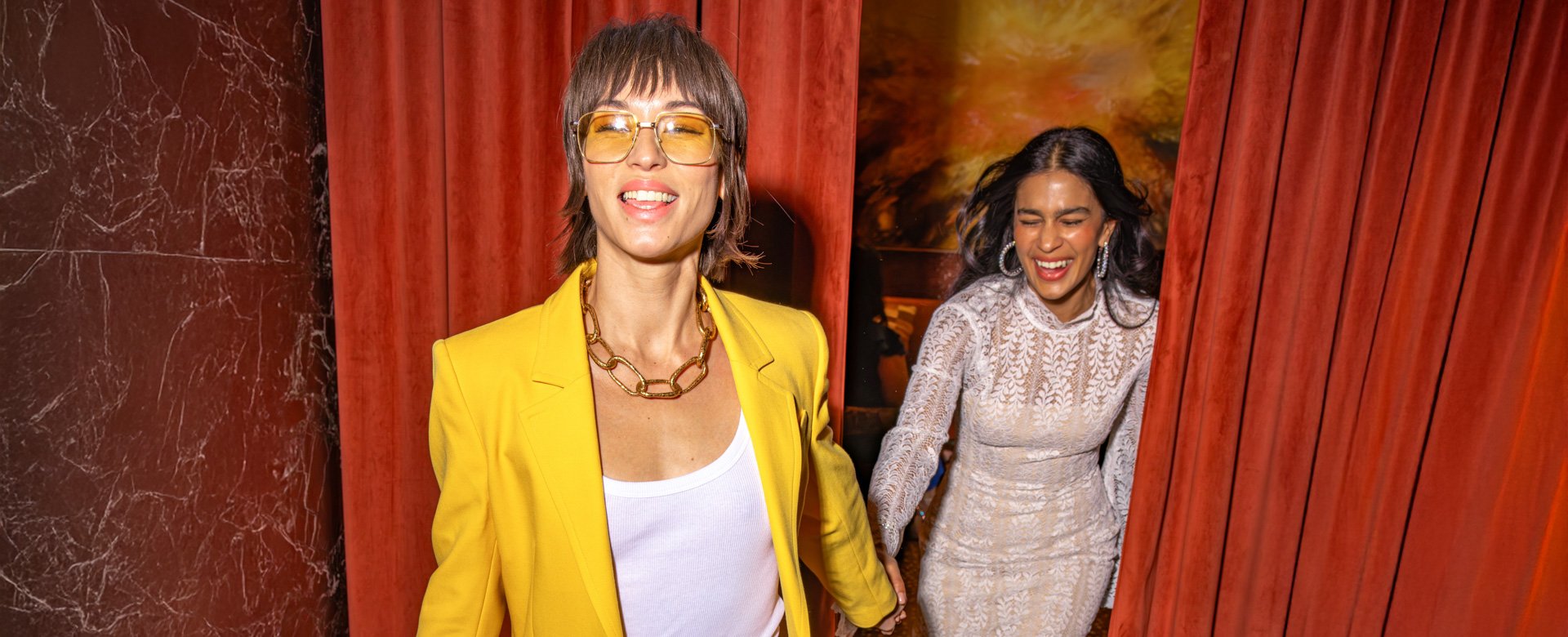 2 women holding hands walking though curtains.