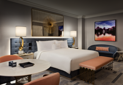 Hotel room example with bed, couch, table and art.