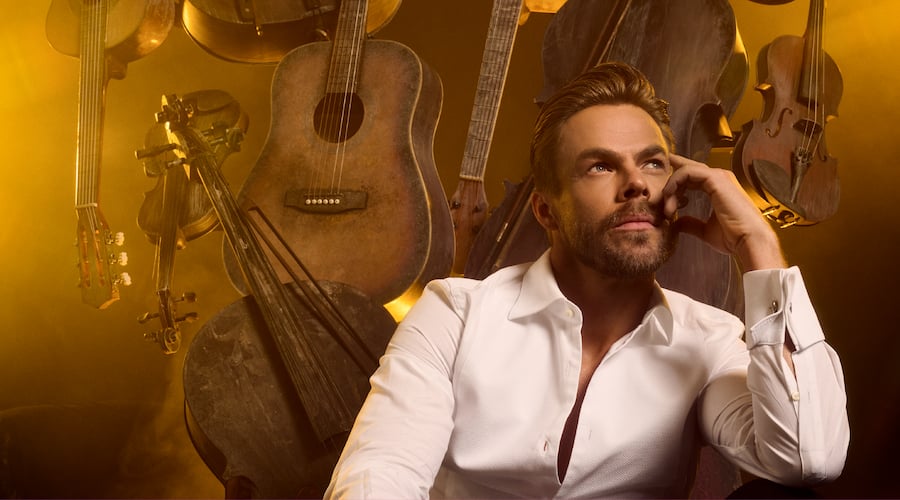 Derek Hough looking off into the distance in front of stringed instruments