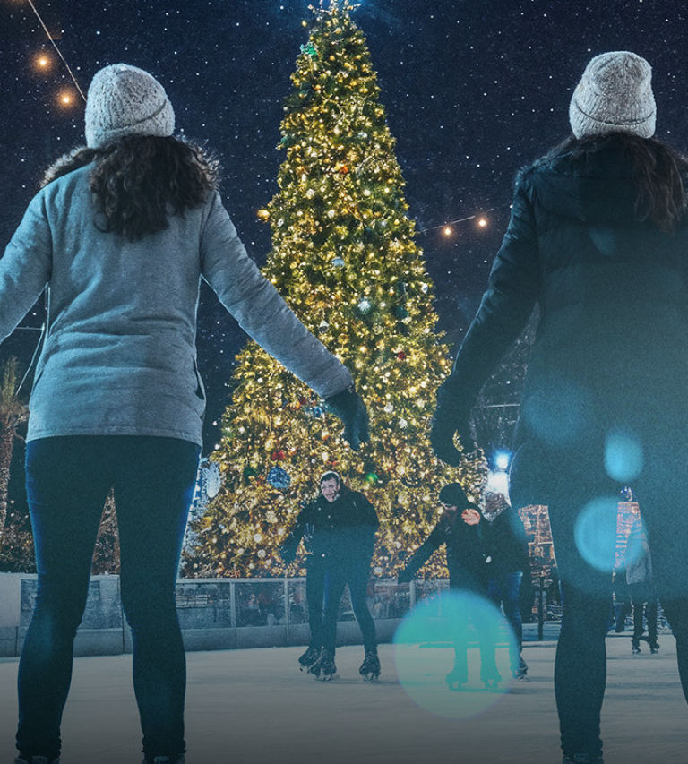 People on ice skates looking at a holiday tree
