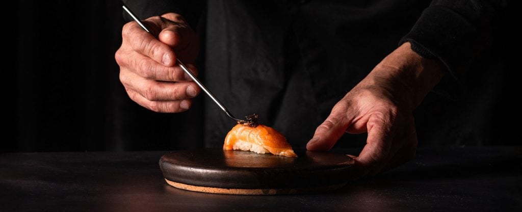 Hands placing caviar on salmon piece