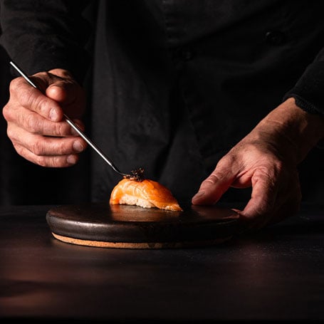 Hands placing caviar on salmon piece