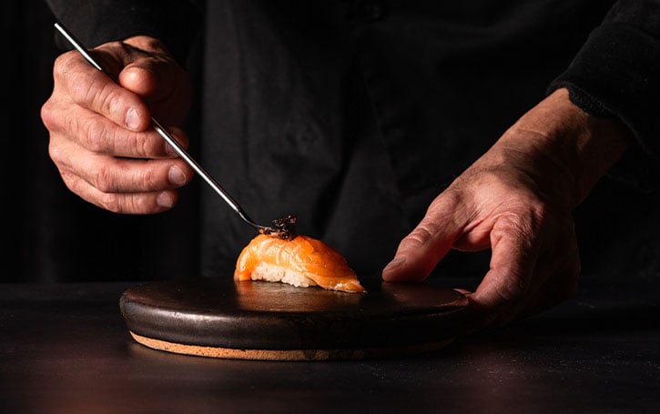 Hands placing caviar on salmon piece