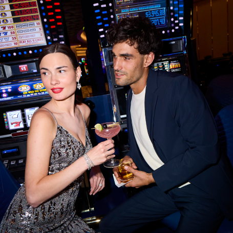Man and woman sitting in front of slot machines holding drinks