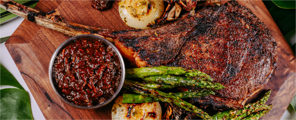 Steak sitting on wooden block with asparagus, onions, and sauce.