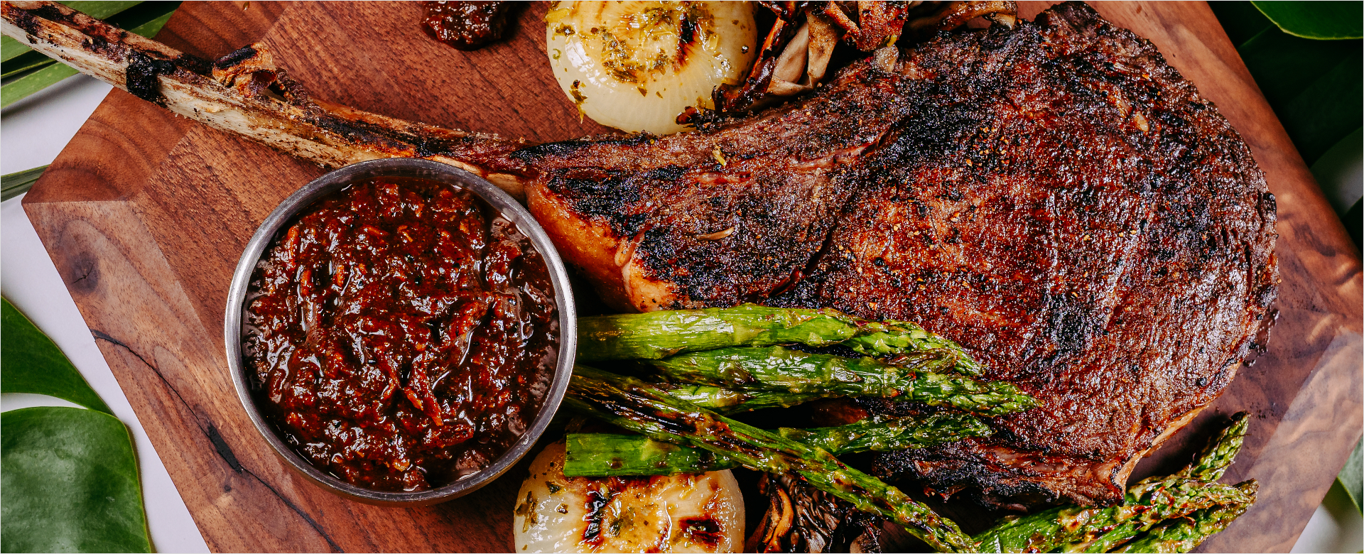 Steak sitting on wooden block with asparagus, onions, and sauce.