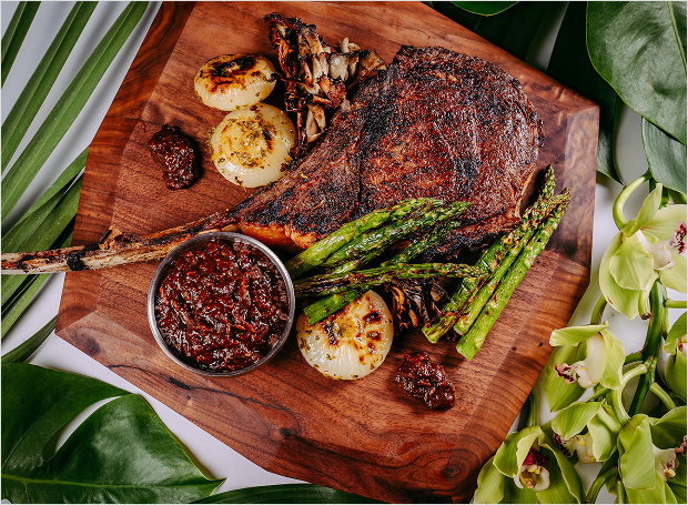 Steak sitting on wooden block with asparagus, onions, and sauce.
