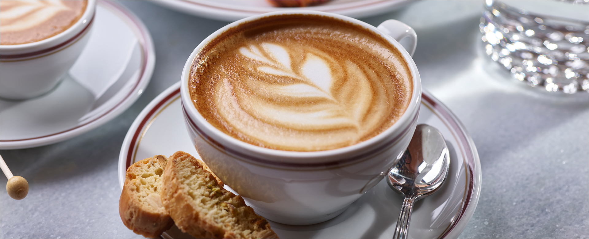 Latte with flowered design sitting on plate with bread and spoon