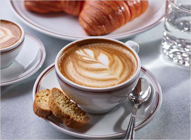 Latte with flowered design sitting on plate with bread and spoon