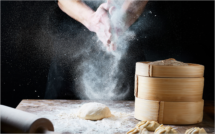 Hands clapping with flour over a table with dough, rolling pin and dumpling holder