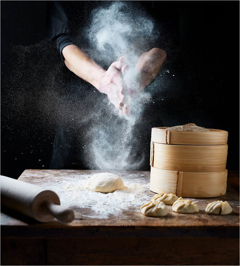 Hands clapping with flour over a table with dough, rolling pin and dumpling holder