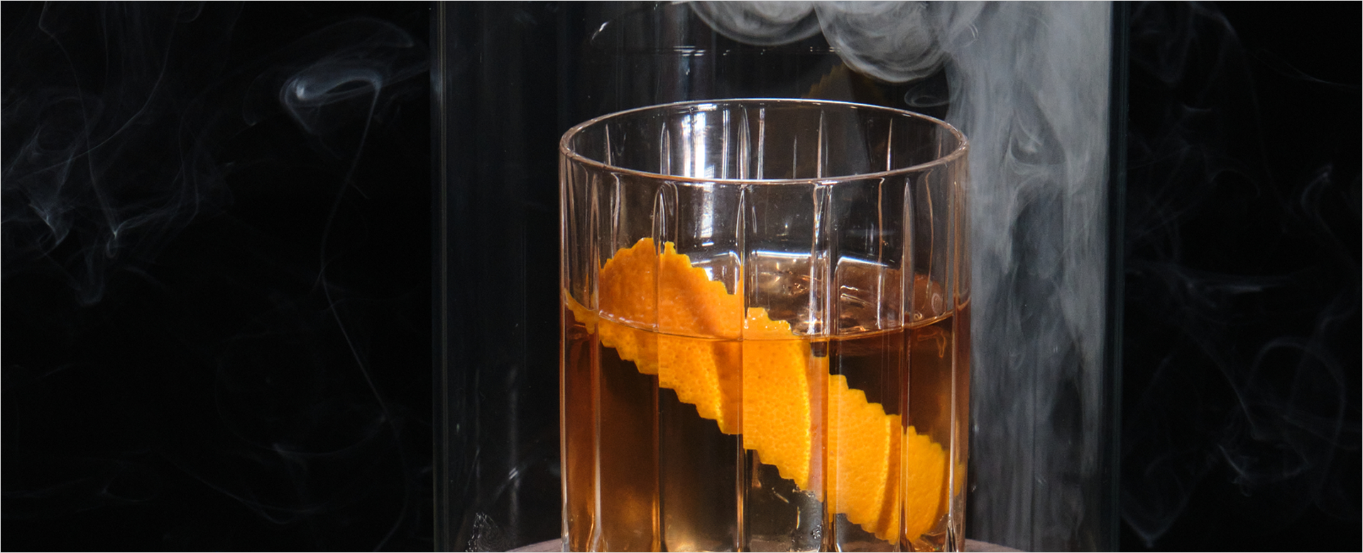 Glass of amber liquid with orange garnish with smoke
