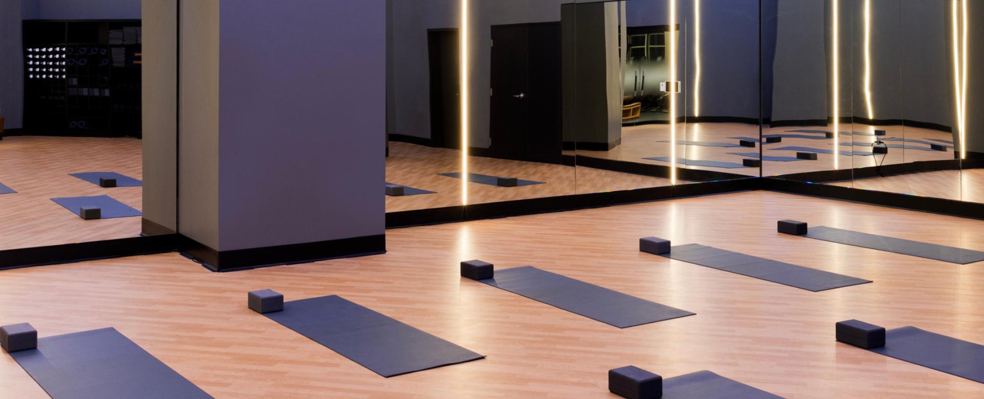Modern fitness studio with yoga mats and blocks arranged on a wood floor in front of mirrored walls.