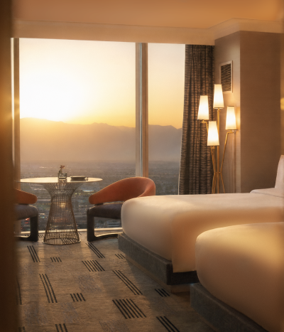Relaxing warm Fall sunset view from beautiful room overlooking the Las Vegas Strip with two queen beds, table with floor to ceiling windows and dim lit lights