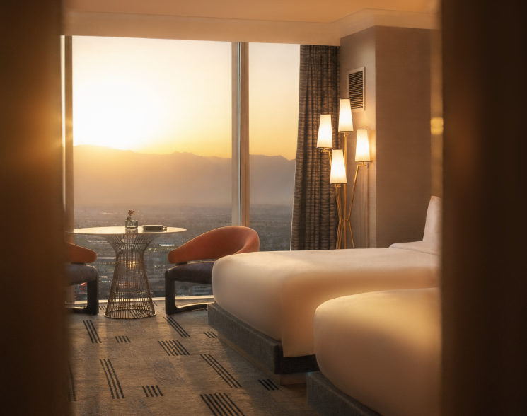 Relaxing warm Fall sunset view from beautiful room overlooking the Las Vegas Strip with two queen beds, table with floor to ceiling windows and dim lit lights