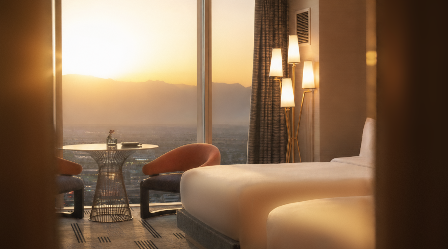 Relaxing warm Fall sunset view from beautiful room overlooking the Las Vegas Strip with two queen beds, table with floor to ceiling windows and dim lit lights
